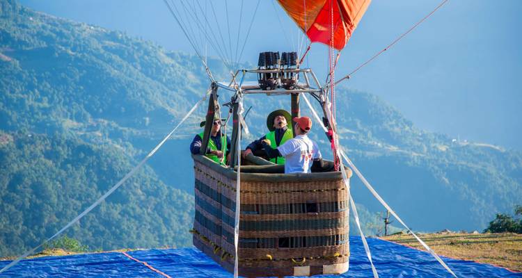 Menschen in einem Heißluftballonkorb bereiten sich auf den Start vor, mit Bergen im Hintergrund.