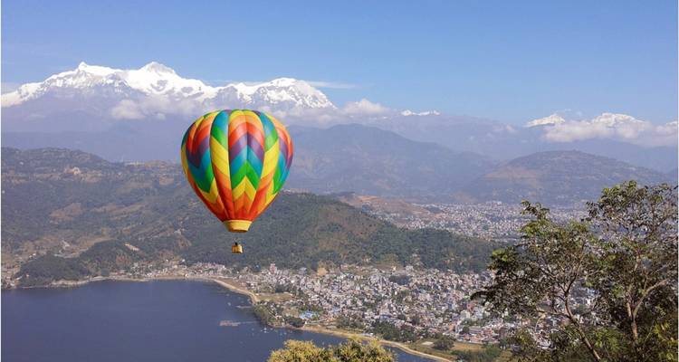 Bunter Heißluftballon über einem Tal mit Bergen im Hintergrund.