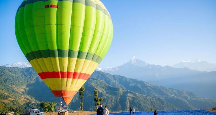 Grüner und gelber Heißluftballon mit Menschen, die sich in einer bergigen Gegend auf den Start vorbereiten.