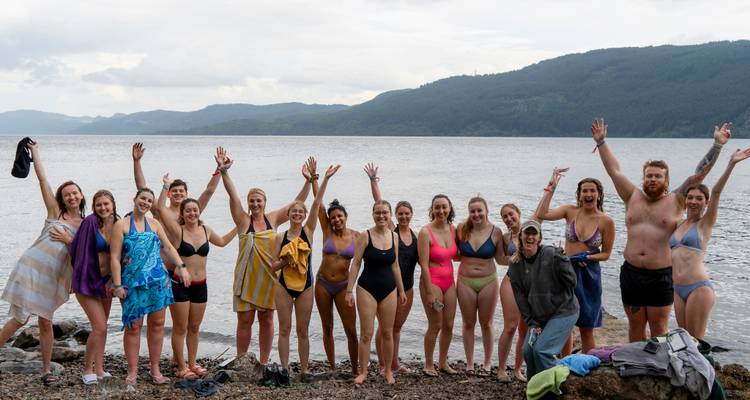 Group posing in swimwear by a lake.