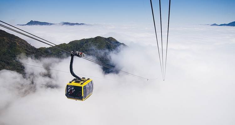 Teleférico balanceándose sobre un mar de nubes con un telón de fondo montañoso.