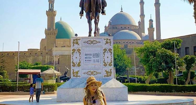 Eine Frau posiert vor einer Statue und Moschee in einer Stadtlandschaft.