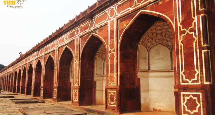 Une longue rangée d'arches en grès rouge avec des motifs incrustés blancs complexes dans un monument moghol.