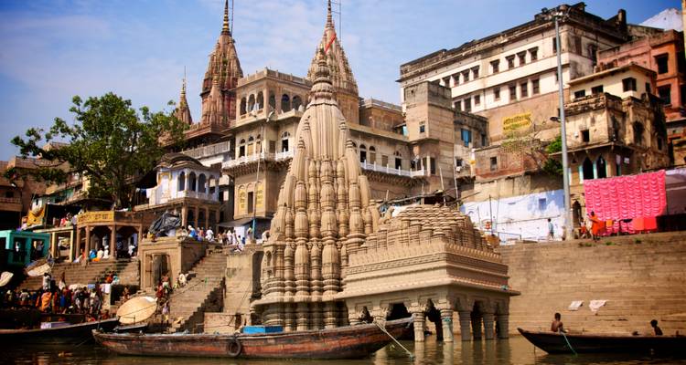 Des temples et des bâtiments anciens bordent les ghats du Gange avec des bateaux et des gens rassemblés le long de l'eau à Varanasi.