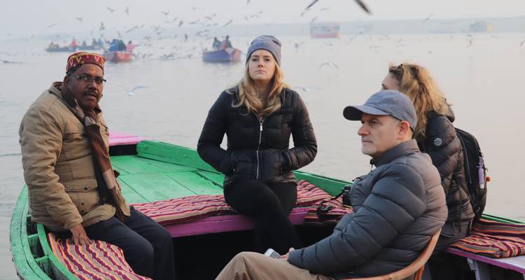 Des touristes sont assis dans un bateau en bois coloré sur une rivière brumeuse tandis que des mouettes volent au-dessus.