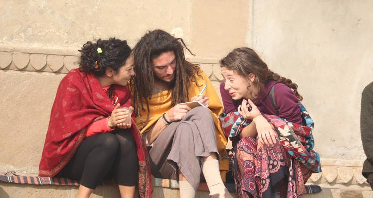 Trois jeunes routards assis sur un muret discutent en regardant un téléphone.