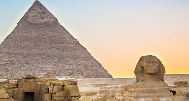 Gran Esfinge de Giza con una pirámide al fondo al atardecer.