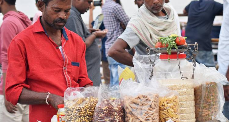 Straßenhändler ordnet bunte Snacks und Getreide an einem belebten indischen Marktstand an.
