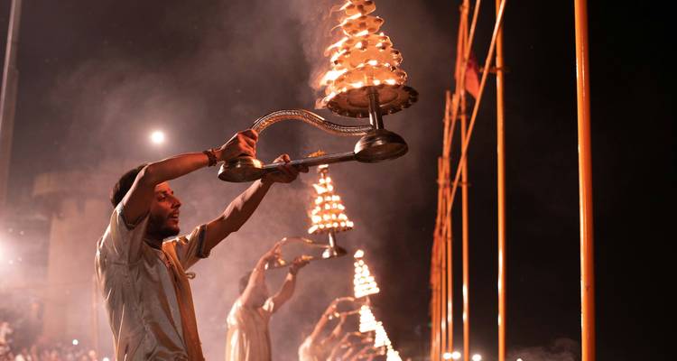 Priester führen nachts die Ganga-Aarti-Zeremonie durch und halten mehrstufige Öllampenständer hoch.