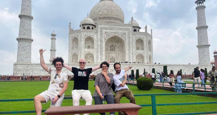 Quatre voyageurs posent avec énergie sur un banc avec le Taj Mahal majestueusement derrière eux.
