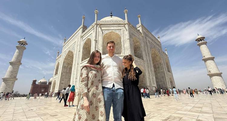 Trois visiteurs se tiennent devant le Taj Mahal en marbre blanc étincelant sous un ciel bleu dégagé.