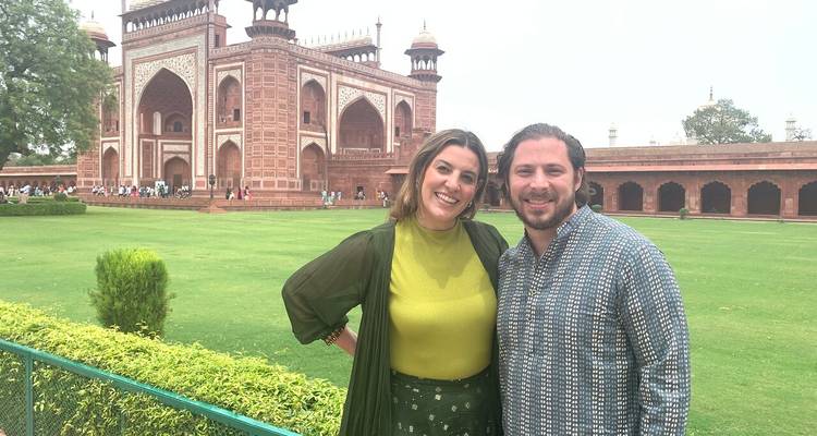 Un couple souriant se tient devant la porte ornée en grès rouge du complexe du Taj Mahal.