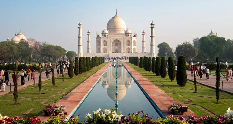 Ikonische Frontansicht des Taj Mahal mit perfekter Spiegelung im langen Wasserbecken und Besuchern entlang des Weges.