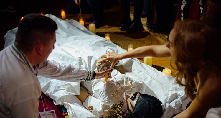 Les invités reconstituent un rituel dramatique autour d'une silhouette voilée avec des bougies au sol.
