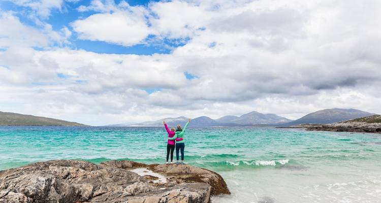 Pareja de pie sobre rocas contemplando un mar azul.