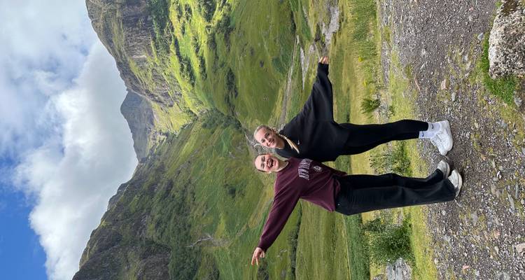 Dos amigos posando en medio de un paisaje montañoso dramático bajo cielos brillantes.