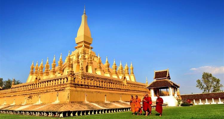 Monks walking by a gold stupa under a bright blue sky.