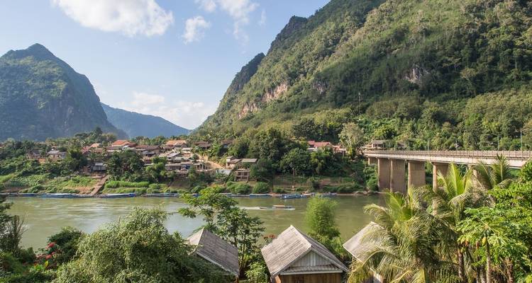 A picturesque village by a river with mountains on both sides.