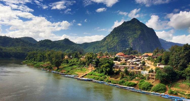 A serene riverside village with mountains in the background.