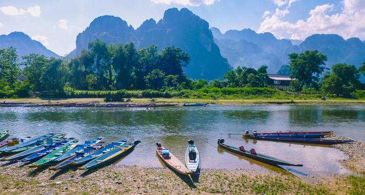 Colorful boats lined up along a scenic river with mountainous backdrop.