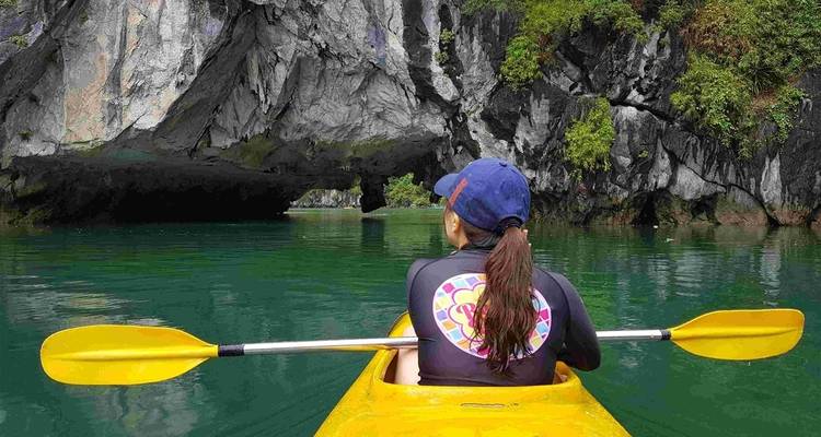 A woman kayaking through calm waters under a rock arch.