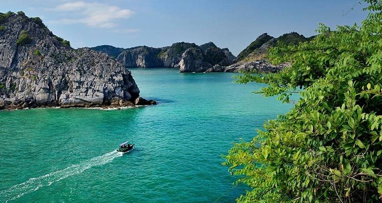 Aguas verde brillante rodeadas de acantilados verde exuberantes, con un pequeño bote a la distancia.