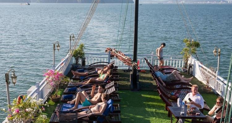 Personas relajándose en sillas de cubierta en la cubierta de un barco con vistas panorámicas de la bahía.