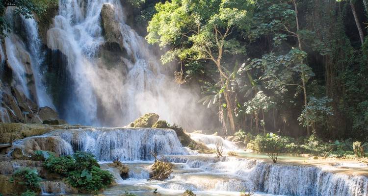 Waterfall flowing down multiple picturesque levels with sunlight filtering through trees.