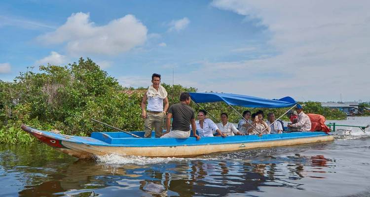 People riding a boat on a body of water with vegetation in the background.