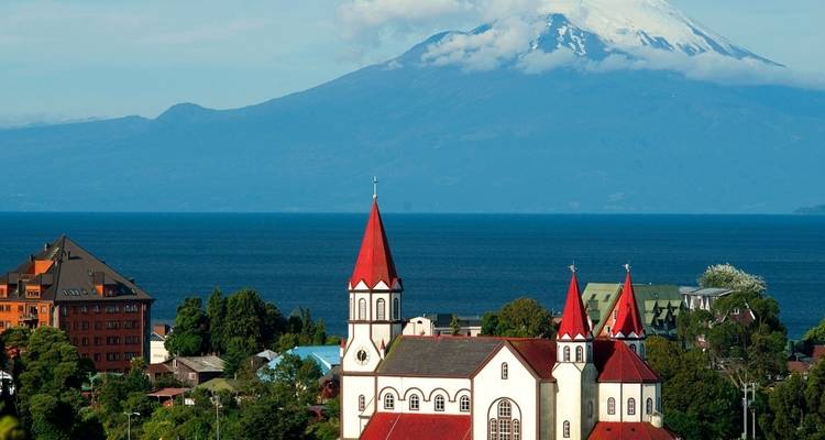 Une église aux toits rouges devant un lac et un volcan.
