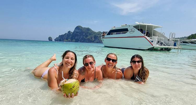 Quatre femmes posant avec une noix de coco dans une eau peu profonde et claire.