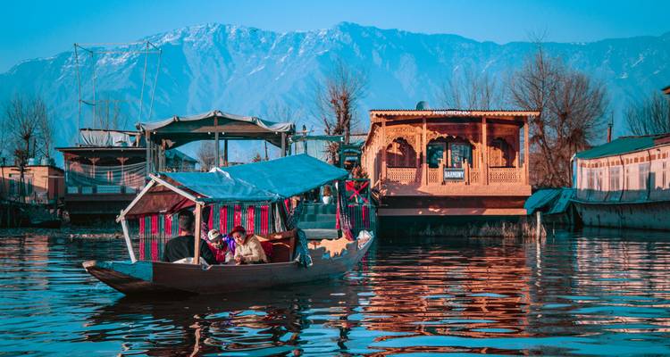Kleurrijke shikara boot glijdt over Dal Lake tegen besneeuwde bergen en traditionele houten woonboten.