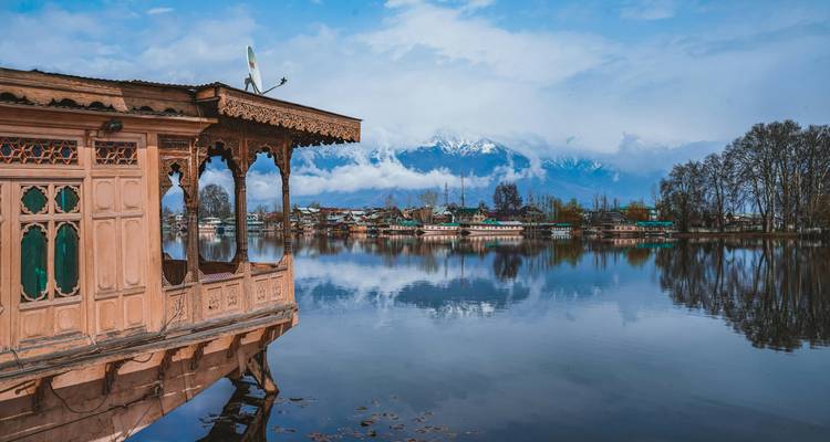 Traditionele gesneden houten woonboot op het stille Dal Lake met gespiegelde reflecties van verre besneeuwde bergen.
