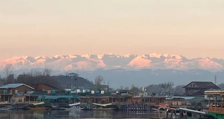Serene Dal Lake woonboten bij dageraad met roze getinte Himalaya bergketen op de achtergrond.
