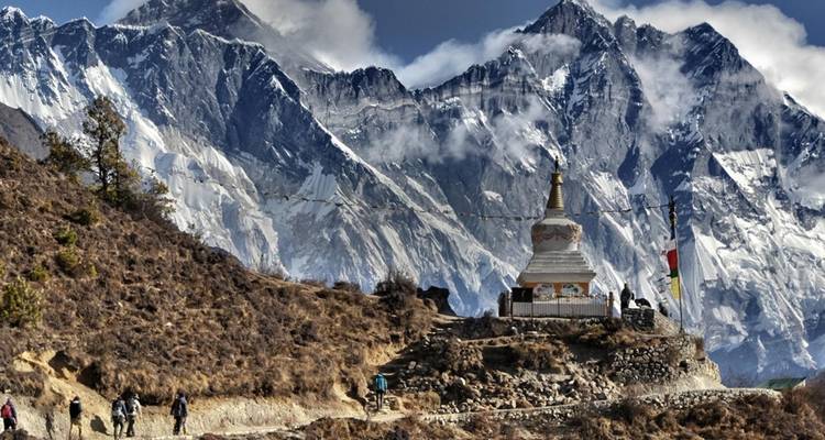 Stupa bouddhiste avec drapeaux de prière devant des pics montagneux imposants.