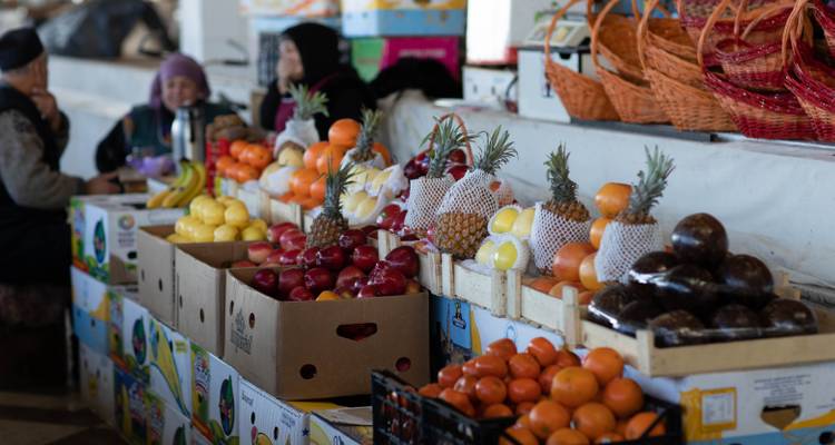 Marktstand mit bunt aufgetürmten Früchten und plaudernden Händlern