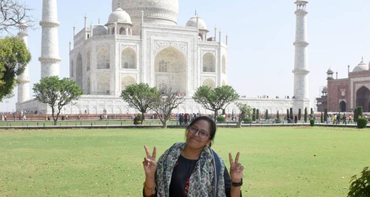 Jonge vrouw die vredestekens maakt voor de glinsterende gevel en verzorgde tuinen van de Taj Mahal.