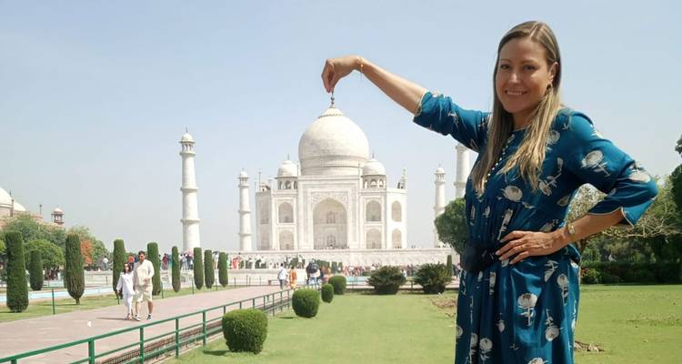 Vrouwelijke reiziger die speels de koepel van de Taj Mahal van afstand wegknijpt in een geforceerde perspectief pose.