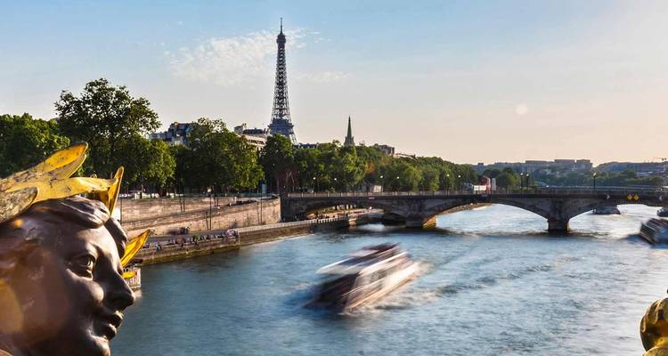 Barco de crucero borroso avanza a velocidad por el Sena con la Torre Eiffel y un puente ornamentado bajo la luz del atardecer.