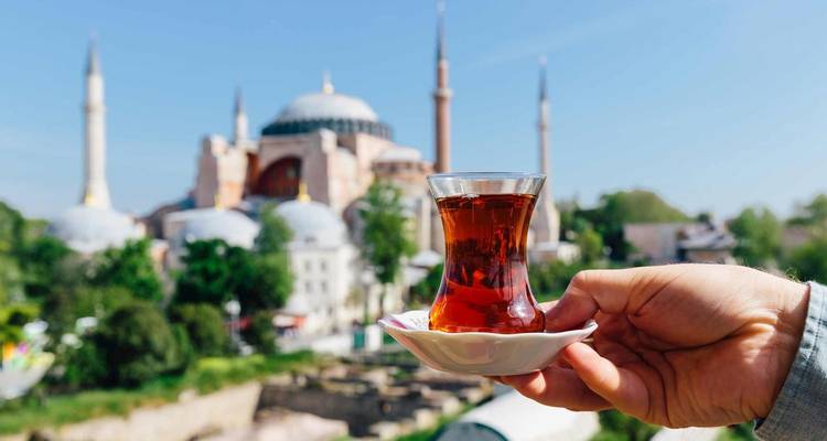 Verre de thé tenu en l'air avec une vue sur Sainte-Sophie à Istanbul.