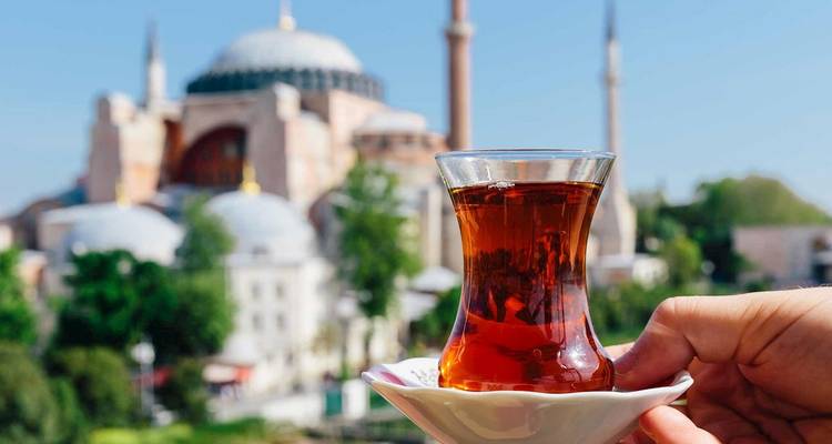 Verre à tulipe traditionnel de thé turc tenu en l'air avec la silhouette floue de Sainte-Sophie en arrière-plan
