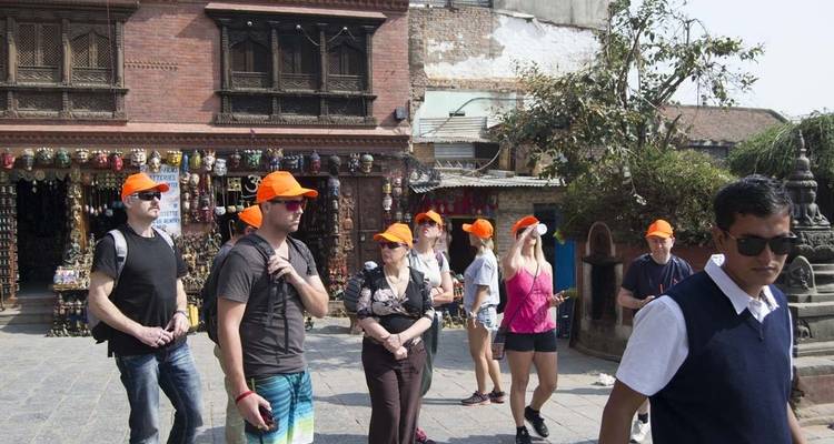 Des touristes avec des chapeaux oranges explorant une place ouverte avec des boutiques.