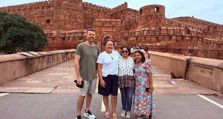 Small group of travelers smile on a stone bridge before massive red-sandstone fortress walls.