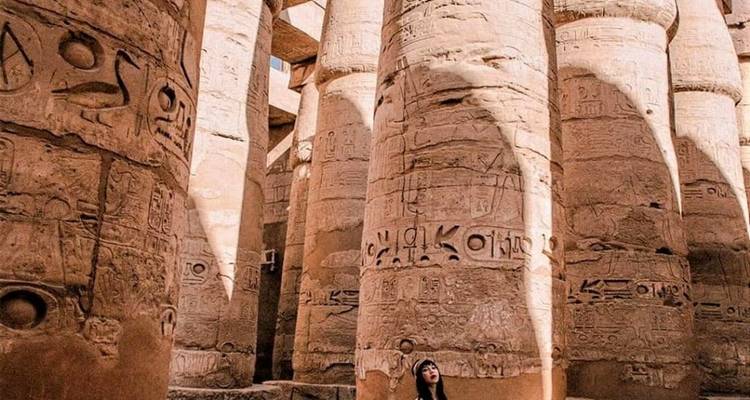 Een vrouw omringd door torenhoge antieke zuilen met hiërogliefen.