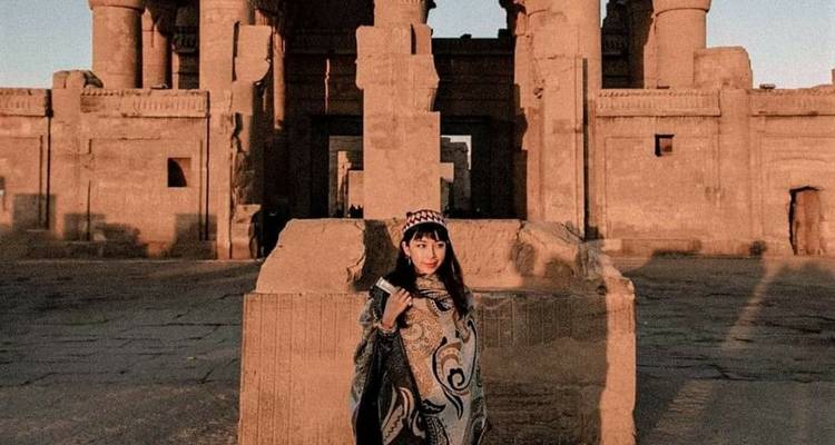 Een vrouw in traditionele kleding staat voor een oude tempel.