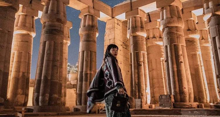 Een vrouw staat tussen de goed verlichte zuilen van een oude tempel.