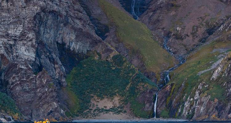 Des falaises rocheuses escarpées avec des parcelles de mousse verte et des cascades étroites se jetant dans une crique rocheuse.