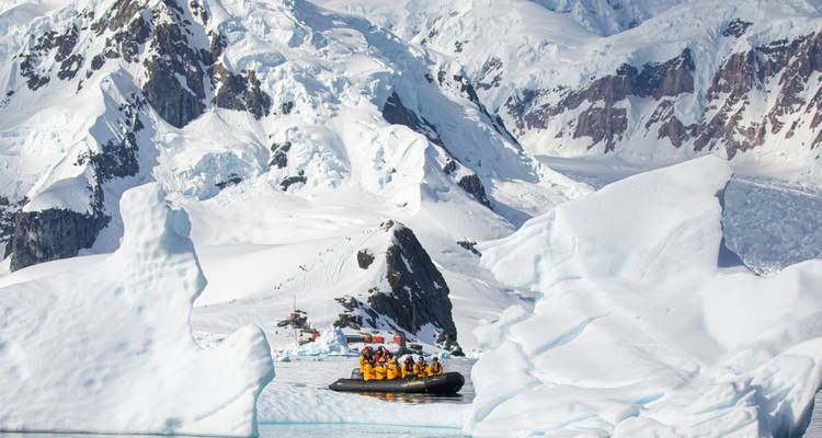 Zodiacs remplis d'aventuriers vêtus de gilets jaunes naviguant entre les icebergs antarctiques imposants et les pics enneigés.