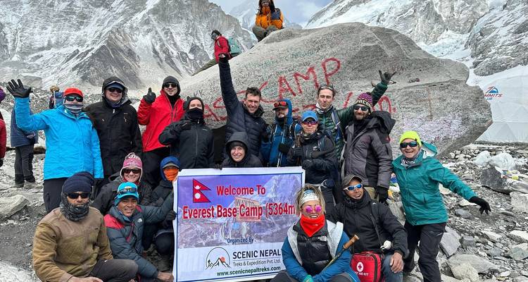 Grupo emocionado de trekking posando con el cartel 'Everest Base Camp 5364m' al lado de la famosa roca y el glaciar.