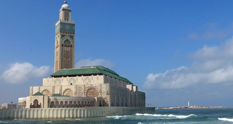 Eine große Moschee mit einem hohen Minarett am Meer unter einem strahlend blauen Himmel.
